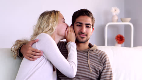 Blonde-whispering-a-secret-to-her-boyfriend-on-the-couch-