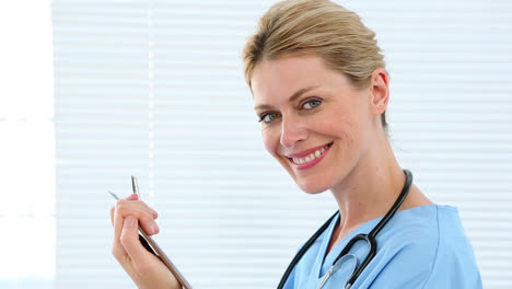 Nurse-holding-clipboard-smiling-at-camera