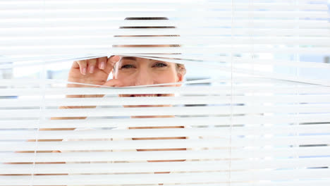 Smiling-businesswoman-peeking-through-the-blinds
