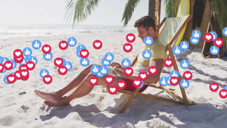Animation-of-red-heart-love-and-like-digital-icons-over-man-in-deckchair-with-laptop-on-beach