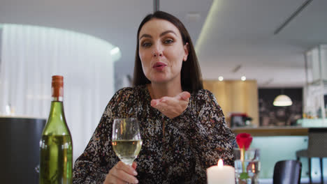 Kaukasische-Frau-Beim-Romantischen-Abendessen-Im-Restaurant,-Hält-Ein-Weinglas-Und-Bläst-Der-Kamera-Einen-Kuss
