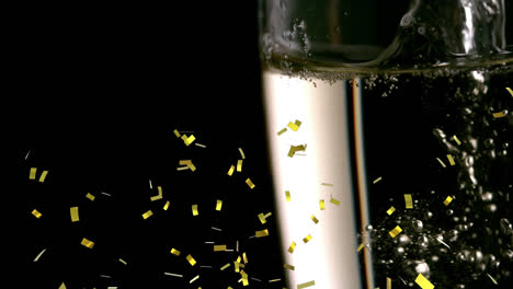 Golden-confetti-falling-over-close-up-of-champagne-bubbles-in-a-glass-against-black-background