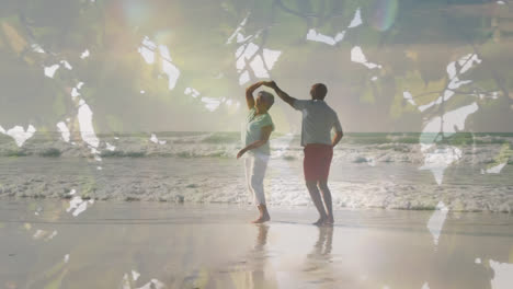Animation-of-glowing-light-over-happy-senior-couple-dancing-by-seaside