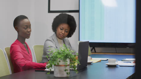 Two-african-american-businesswomen-talking-at-office-meeting,-one-holding-paperwork