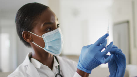 African-american-female-doctor-wearing-face-mask-preparing-covid-vaccine-for-patient