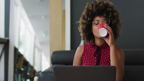 Mixed-race-woman-going-through-paperwork-drinking-coffee-using-laptop-in-the-office
