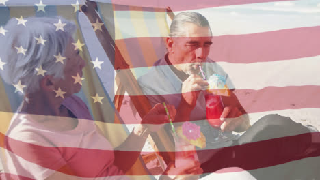 Animation-Einer-Amerikanischen-Flagge,-Die-über-Einem-älteren-Paar-In-Liegestühlen-Weht,-Das-Am-Strand-Etwas-Trinkt