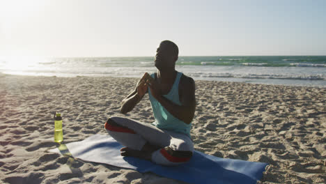 Focused-african-american-man-practicing-yoga-on-beach,-exercising-outdoors-by-the-sea