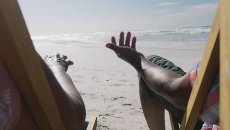 Älteres-Afroamerikanisches-Paar-Sitzt-Auf-Sonnenliegen-Und-Hält-Händchen-Am-Strand