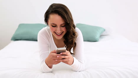 Lächelnde-Frau,-Die-Auf-Dem-Bett-Liegt-Und-Auf-Ihrem-Telefon-SMS-Schreibt