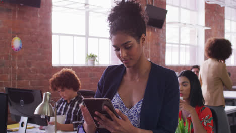 Mixed-race-businesswoman-using-tablet-in-office-with-diverse-colleagues-in-background