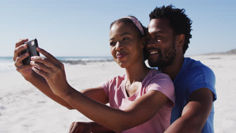 African-american-couple-smiling-taking-selfie-with-smartphone-on-the-beach