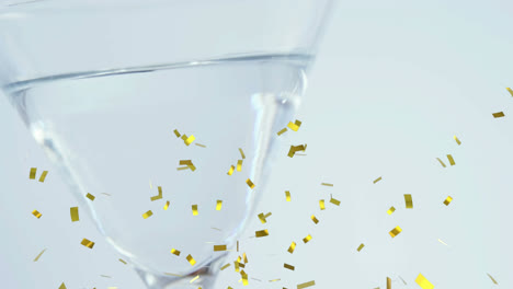 Golden-confetti-falling-over-close-up-of-olives-falling-into-cocktail-glass-against-grey-background
