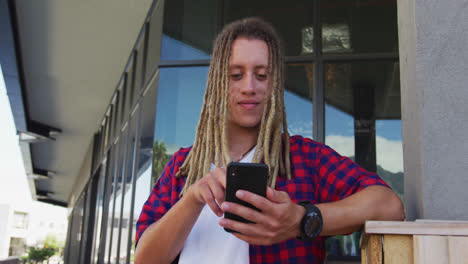 Mixed-race-man-with-dreadlocks-sitting-at-table-outside-cafe-using-smartphone