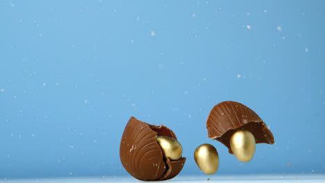 Animation-of-chocolate-easter-egg-falling-and-breaking-open-with-gold-eggs,-on-blue-background