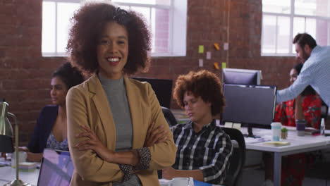 Mixed-race-businesswoman-sitting-smiling-in-office-room-with-diverse-colleagues-in-background