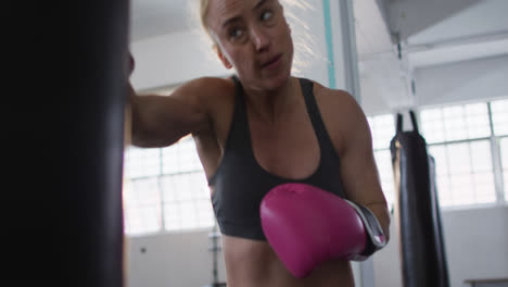 Caucasian-female-boxer-wearing-boxing-gloves-training-with-punching-bag-at-the-gym