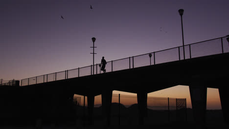 Silhouette-Eines-Mannes,-Der-Abends-über-Eine-Brücke-Läuft