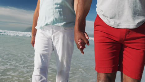 Midsection-of-senior-african-american-couple-walking-and-holding-hands-at-the-beach