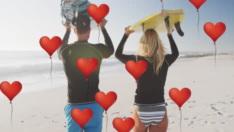 Animation-of-red-heart-love-balloons-digital-icons-over-couple-carrying-surfboards-on-beach