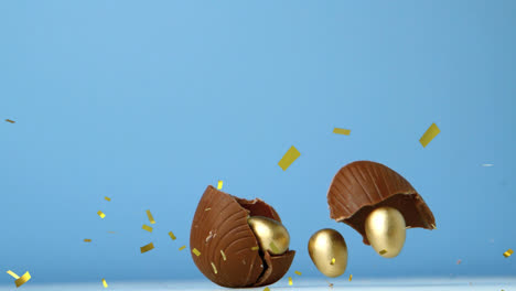 Animación-De-Confeti-Dorado-Sobre-Huevos-De-Pascua-De-Chocolate-Rompiéndose,-Con-Huevos-Dorados-En-Su-Interior,-En-Azul.