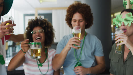 Diverse-group-of-happy-friends-celebrating-st-patrick's-day-drinking-beers-making-a-toast-at-a-bar