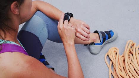 Caucasian-woman-checking-smartwatch-preparing-for-climb-at-indoor-climbing-wall
