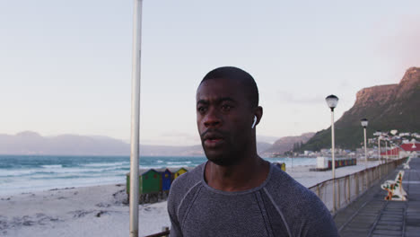 Fokussierter-Afroamerikanischer-Mann,-Der-Im-Freien-Trainiert-Und-Am-Meer-Entlang-Läuft-Und-Dabei-Kabellose-Kopfhörer-Trägt
