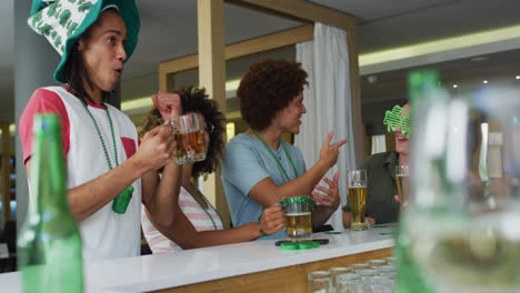 Diverse-group-of-happy-friends-celebrating-st-patrick's-day-drinking-beers-at-a-bar