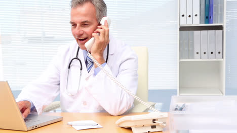 Doctor-talking-on-phone-and-using-laptop-at-his-desk