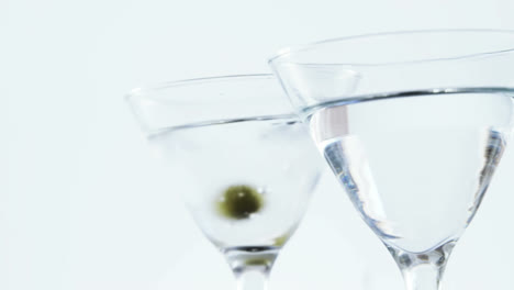 Animation-of-red-specks-moving-over-cocktail-glasses-with-olives-on-white-background