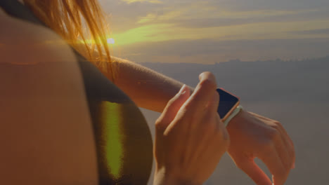 Animation-of-glowing-light-over-sporty-woman-checking-smartwatch-by-sea