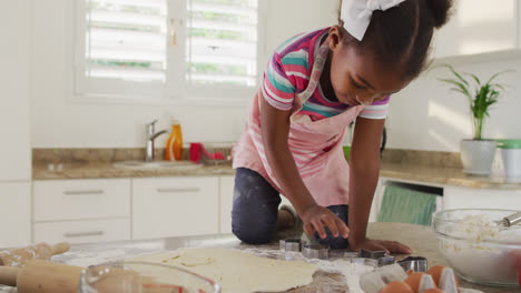 Happy-african-american-girl-using-cookie-cutters-in-kitchen