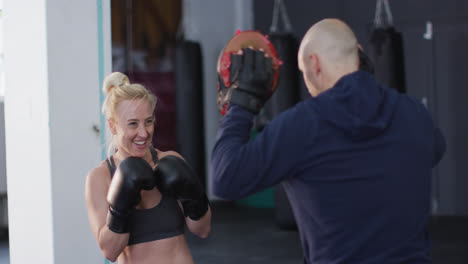 Caucasian-female-boxer-wearing-boxing-gloves-training-her-punches-with-male-trainer-at-the-gym