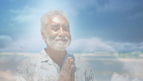 Animation-of-glowing-light-over-portrait-of-happy-senior-man-practicing-yoga-by-seaside