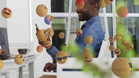 Múltiples-Emojis-De-Cara-Flotando-Contra-Un-Hombre-Afroamericano-Usando-Un-Teléfono-Inteligente