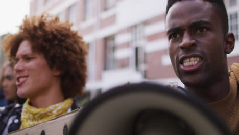 Afroamerikanischer-Mann-Schreit-Mit-Megafon,-Während-Andere-Menschen-Während-Des-Protests-Die-Fäuste-Heben
