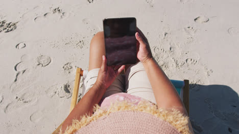 Ältere-Frau-Mit-Gemischter-Abstammung,-Die-Auf-Der-Sonnenliege-Sitzt-Und-Am-Strand-Ein-Smartphone-Benutzt