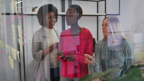 Drei-Unterschiedliche-Geschäftsfrauen-Beim-Brainstorming-Mit-Notizzetteln-An-Der-Glaswand-Im-Büro