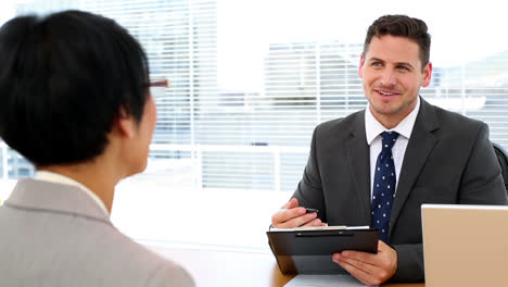 Handsome-businessman-talking-with-interviewee-holding-clipboard