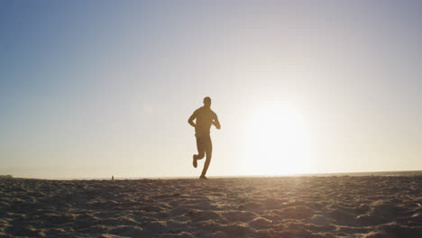 African-american-man-running-on-beach,-exercising-outdoors-in-beach-in-the-evening