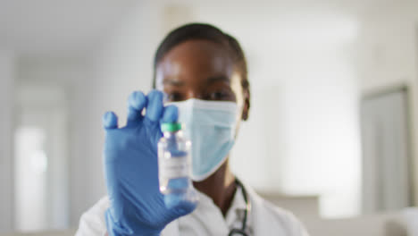 African-american-female-doctor-wearing-face-mask-showing-covid-vaccine-to-camera