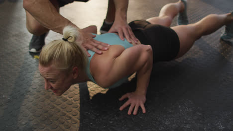 Male-trainer-correcting-form-of-fit-caucasian-woman-while-push-up-exercise-at-the-gym