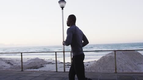 Hombre-Afroamericano-Enfocado-Haciendo-Ejercicio-Al-Aire-Libre,-Corriendo-Junto-Al-Mar