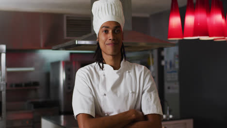 Mixed-race-male-chef-standing-in-kitchen-looking-at-camera-and-smiling