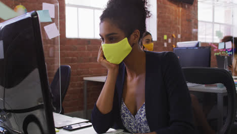 Mixed-race-businesswoman-having-video-chat-sitting-in-front-of-computer-wearing-face-mask