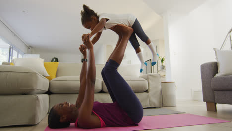 Happy-african-american-mother-and-daughter-doing-yoga-exercise-at-home