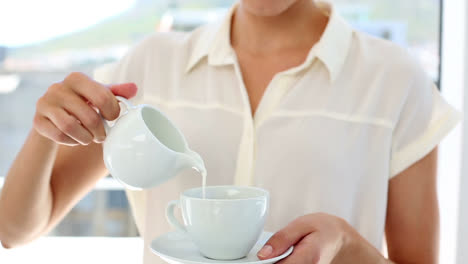 Pretty-businesswoman-pouring-milk-into-cup