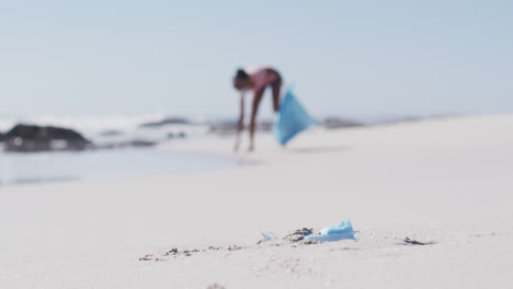 African-american-woman-wearing-holding-rubbish-sack-and-collecting-rubbish-from-the-beach
