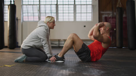 Caucasian-muscular-man-exercising,-doing-sit-ups-with-female-coach